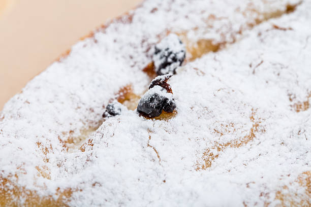Freshly baked apple strudel sprinkled with powdered sugar is served on a plate with vanilla sauce, berries, mint, and pistachios