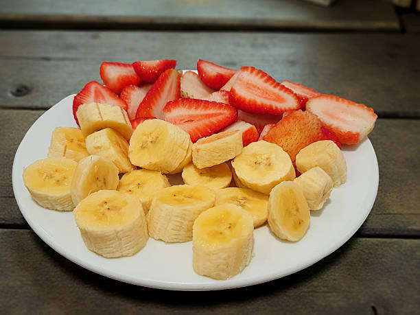 Strawberry and banana cut into slices on a plate on a wooden table.