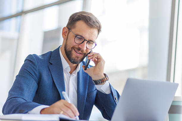 istock Businessman working on laptop and talking on phone in office 2235037875