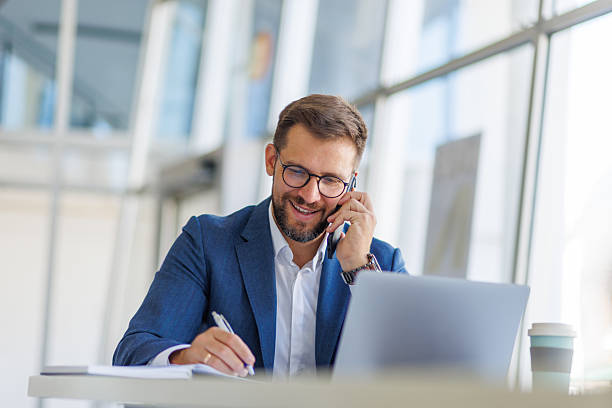 istock Businessman talking on phone and taking notes in modern office 2235037918