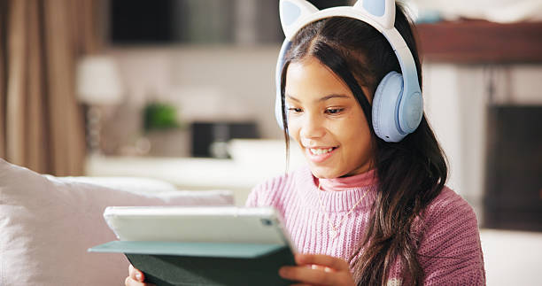 istock Happy, headphones and child on sofa on tablet for elearning, educational games and internet. Relax, weekend and girl on digital tech for watching videos, streaming movies and subscription in home 2235047284