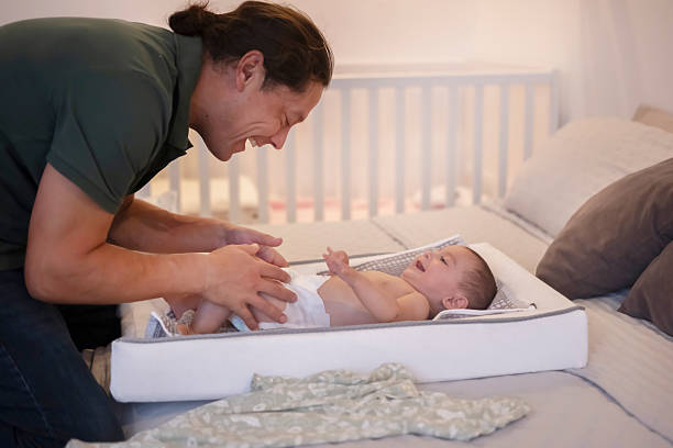 Father happily changing his baby's diaper while lying on a changing table on the bed.