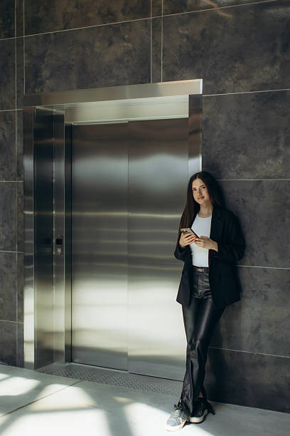 istock Stylish Woman Standing Near Elevator Using Smartphone in Modern Building 2235052443