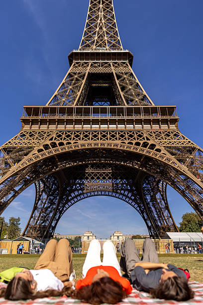 A single mom and her son and daughter are lying on their backs under the Eiffel tower, taking a rest and enjoying the view.