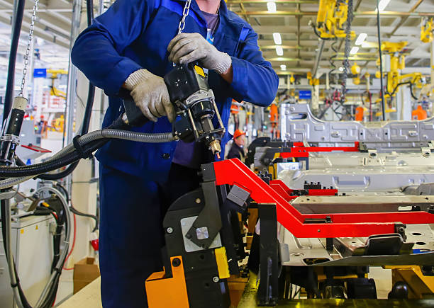 Skilled technicians work on automotive parts using advanced tools and machinery in a busy production hall filled with equipment.