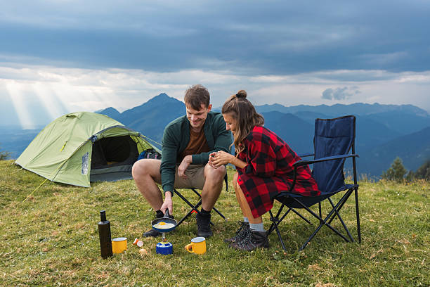 Couple making scrambled eggs on a camping stove, enjoying at a mountain campsite