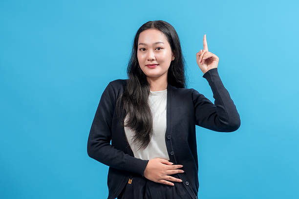 istock Young woman pointing upward with one hand, posing confidently against bright blue background, symbolizing idea, innovation, or emphasis. Perfect for education, communication, and marketing themes. 2235064270