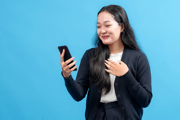 istock Happy young woman using smartphone, smiling with joy, symbolizing connectivity, modern communication, and technology, against a vibrant blue background 2235064311