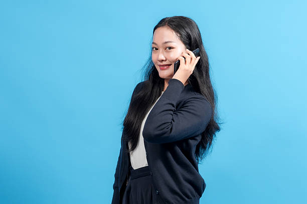 istock Professional woman smiling while talking on smartphone against vibrant blue background. Symbolizes communication, business, connectivity, and modern technology. 2235064390