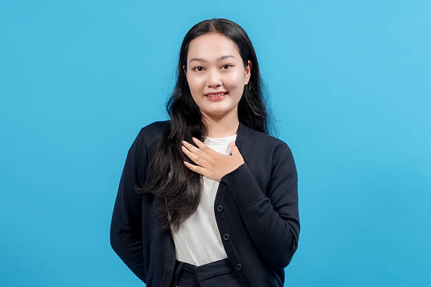 istock Young woman with a sincere expression placing hands on her chest, standing confidently against a solid blue background, conveying gratitude, appreciation, or heartfelt emotion. 2235064652