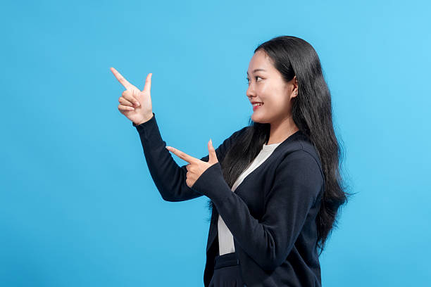 istock Happy woman pointing with both hands to the side against blue background. Confident gesture presenting an idea, perfect for business, advertising, and promotional designs. 2235064704