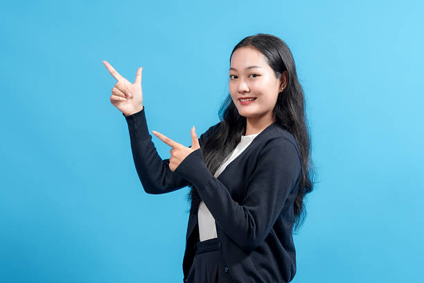istock Smiling woman pointing with both hands against blue background. Positive gesture showing direction or presenting an idea. Perfect for business, marketing, and promotional themes. 2235064711