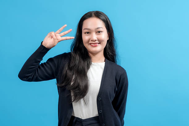 istock Smiling woman looking at the camera, gesturing three fingers with a confident expression, standing against a vibrant blue background. 2235064875