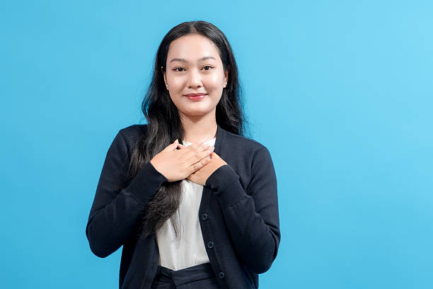 istock Young woman with a sincere expression placing hands on her chest, standing confidently against a solid blue background, conveying gratitude, appreciation, or heartfelt emotion. 2235065170