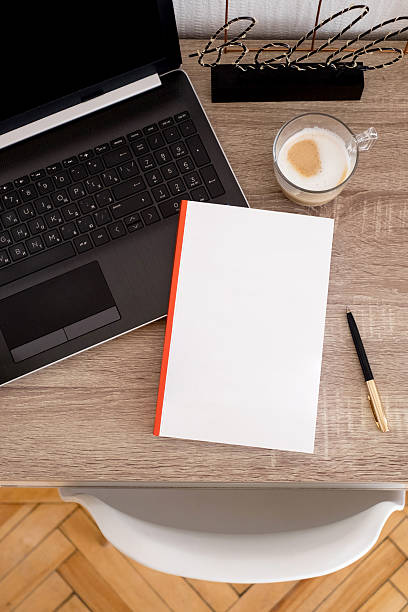 Blank book or notebook mockup on desk with coffee and laptop