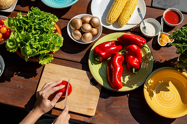 Cutting fresh tomato on a picnic table full of vegetables