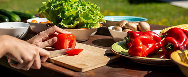 Cutting fresh tomato on a picnic table full of vegetables