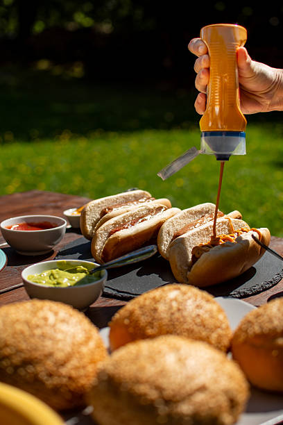 istock Adding mustard on grilled hotdogs on a picnic table 2235082408