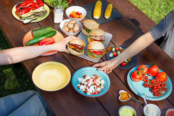 People reaching for Grilled burgers on a picnic table