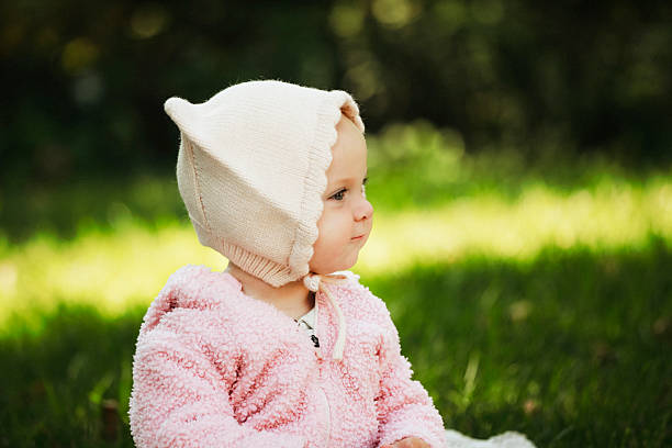 An adorable baby girl, nine months old, sitting in the grass wearing a hat with cat ears. Shot with a Canon 5D Mark IV.