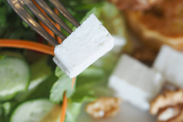 A fork holds a piece of fresh cheese above a vibrant salad with vegetables.