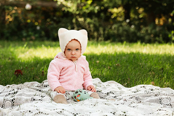 An adorable baby girl, nine months old, sitting in the grass wearing a hat with cat ears. Shot with a Canon 5D Mark IV.