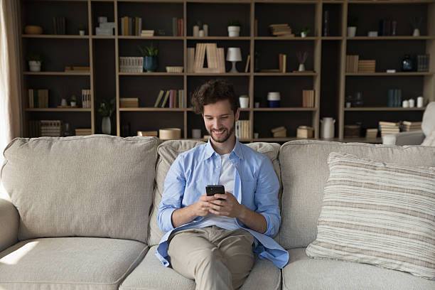 istock Smiling young male using cellphone on comfy couch at home 2235092284
