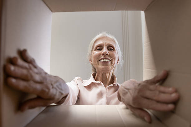 istock Curious smiling senior woman open cardboard package with online order 2235092512