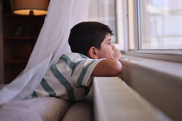 istock Pensive teenage boy looking through a window 2235094109