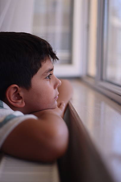 istock Pensive teenage boy looking through a window 2235095204