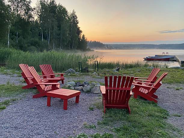 istock Red Adirondack chairs surround a fire pit overlooking a misty lake at dawn. Concept of: Lakeside relaxation. 2235096381