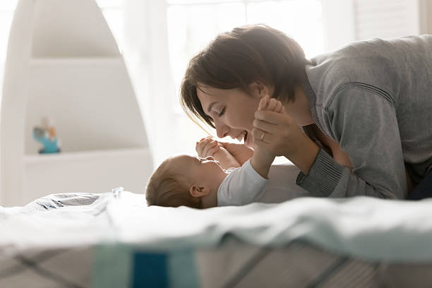 istock Laughing young mom enjoy playing on bed with tiny baby 2235097594