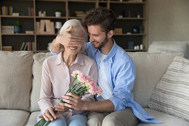 istock Smiling young man present floral gift surprise to elderly mother 2235100051