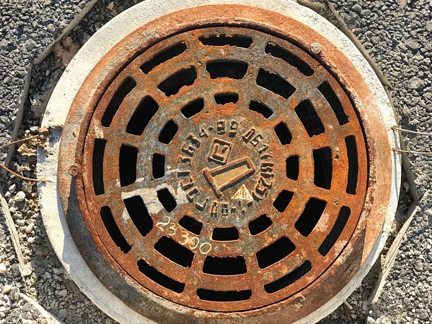 Rusty iron manhole is set into asphalt road surfaces with a large gap at the top in summer season. Close-up