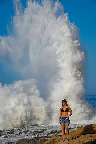 istock PORTRAIT: Rocky beach with pretty woman against colossal wave splash behind her 2235116826