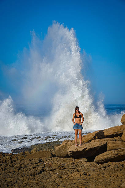 istock PORTRAIT: Woman poses confidently on rocky beach with a splash of a massive wave 2235116836