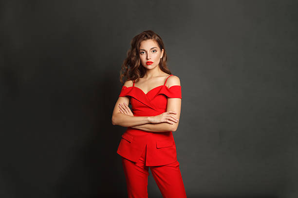 istock Successful young woman in red suit standing against black studio wall background 2235121150