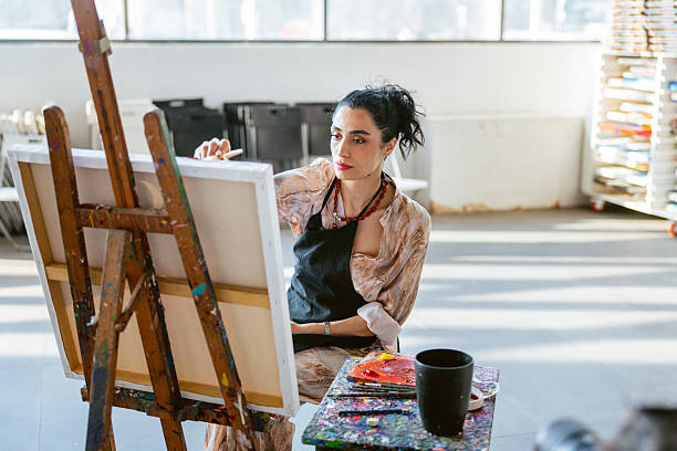 istock Focused Female Artist Painting in Sunlit Studio 2235121491