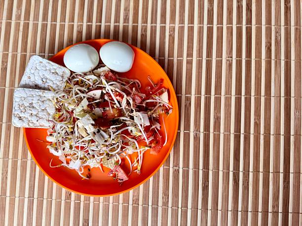 Salad of fresh vegetables and micro-greens. Tomatoes, eggs, bread rolls, onions, apples, mound of sprouted mung beans in an orange bowl on bamboo background. Concept of diet, vegan, healthy products.