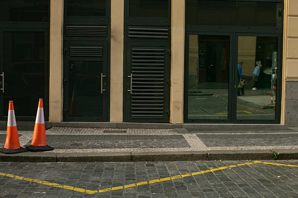 There are two traffic cones that are orange and white in color positioned on the sidewalk right in front of a building structure