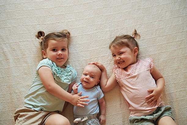 Beautiful children playing in the bedroom. Twin sisters and newborn brother. High angle view.