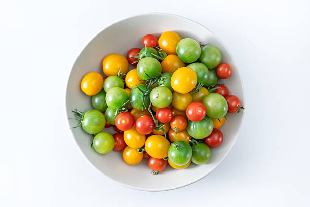 Close-up of a bowl filled with colorful cherry tomatoes in red, yellow, and green shades, showcasing freshness and variety on a clean white background.