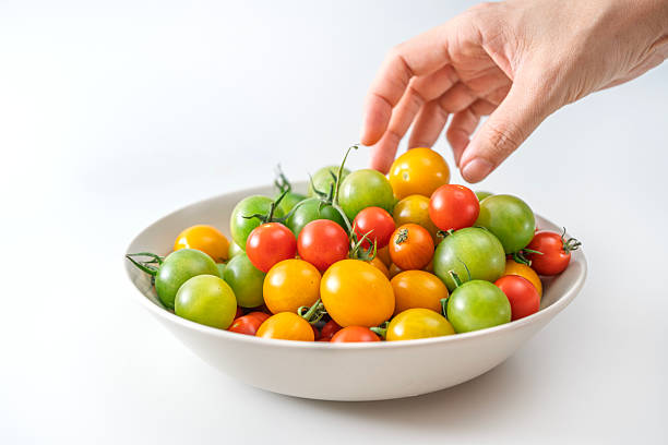Hand picking colorful cherry tomatoes from a bowl on white background