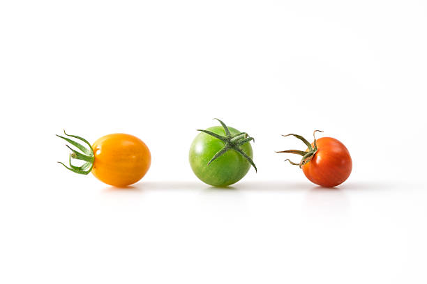 Minimalist composition of three cherry tomatoes in yellow, green, and red colors, arranged in a row to represent different ripeness stages, isolated on a clean white background.
