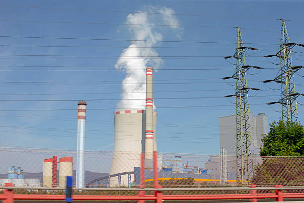 A view of a power plant emitting steam and pollution with power lines in the foreground, showcasing industrial energy production.