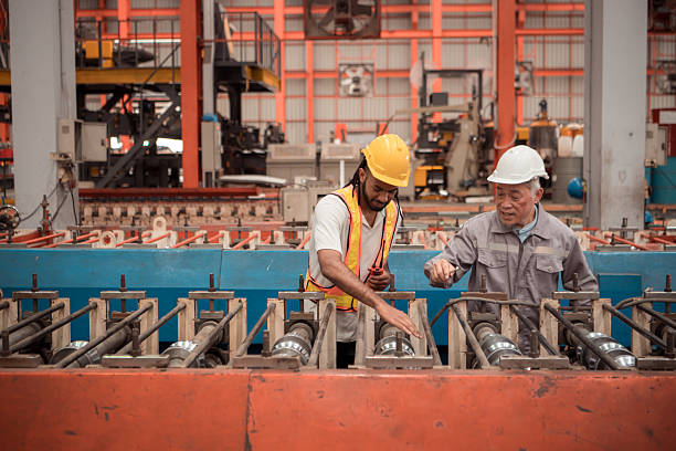 Senior engineers and young man workers are talking and inspecting machines on a production line with safety helmets and other equipment