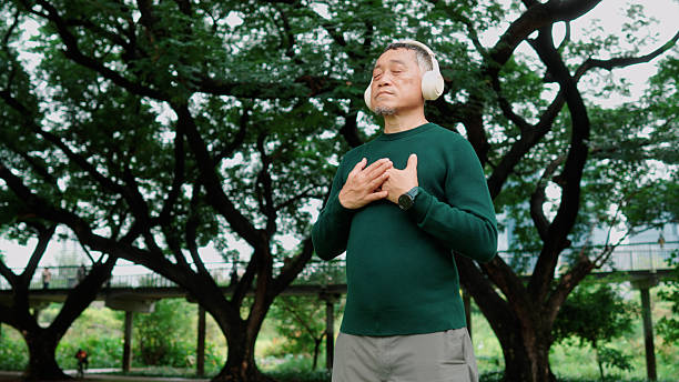 istock Elderly Asian man meditating under a tree with wireless headphones, calm and refreshed 2235158256