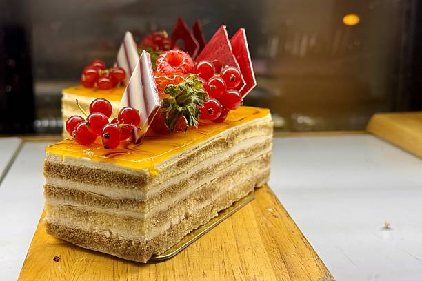 A portion of layered cream yellow cake with red raspberries, red currants on a wooden stand