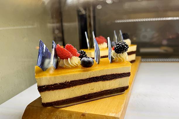 A portion of layered cream yellow cake with red raspberries, blackberries, blueberries on a wooden stand