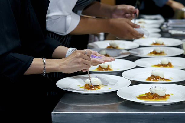 chefs in a professional kitchen garnishing dessert plates with precision. restaurant chef team showcasing fine dining presentation, culinary creativity, and teamwork in food preparation.
